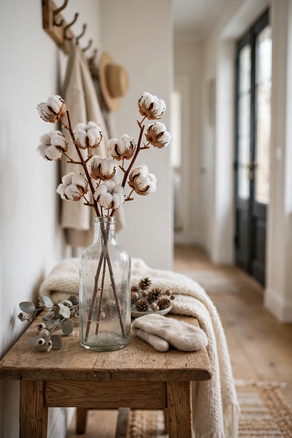Dried cotton stems in an old glass bottle on a wooden entry table